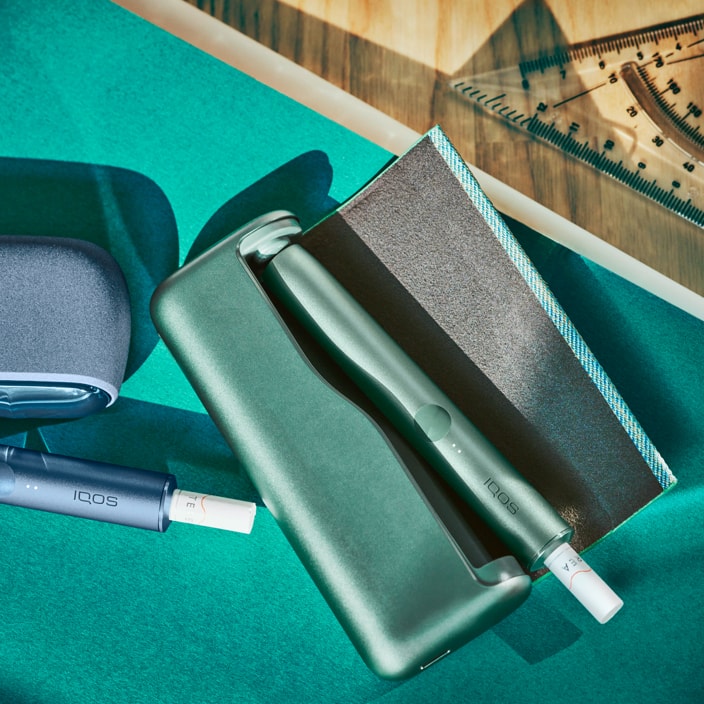 Jade green IQOS ILUMA device and charger on a desk. Jade green IQOS ILUMA device and charger on a desk.