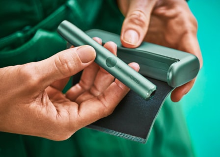 Close up of hands holding IQOS ILUMA jade green device. Close up of hands holding IQOS ILUMA jade green device.
