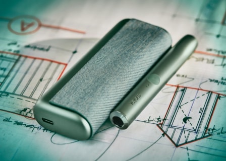 A jade green IQOS ILUMA device rests on a map. A jade green IQOS ILUMA device rests on a map.