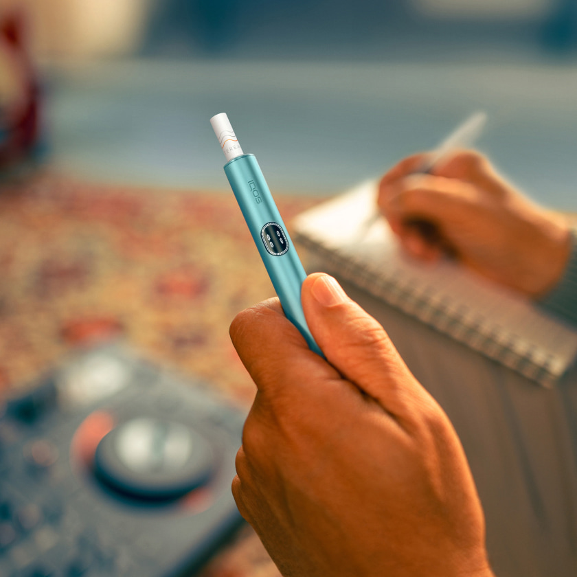  A Jade Green IQOS ILUMA PRIME Holder and Pocket Charger in a persons hands.