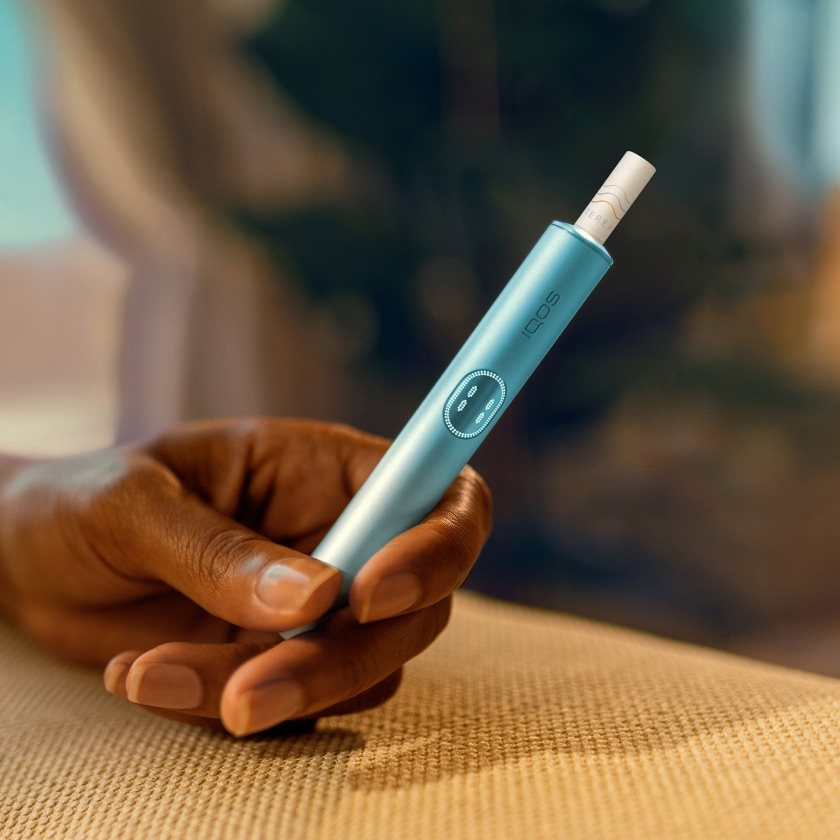 مستندات السفر وهاتف محمول وجهاز IQOS ILUMA PRIME وشاحن جيب على طاولة.