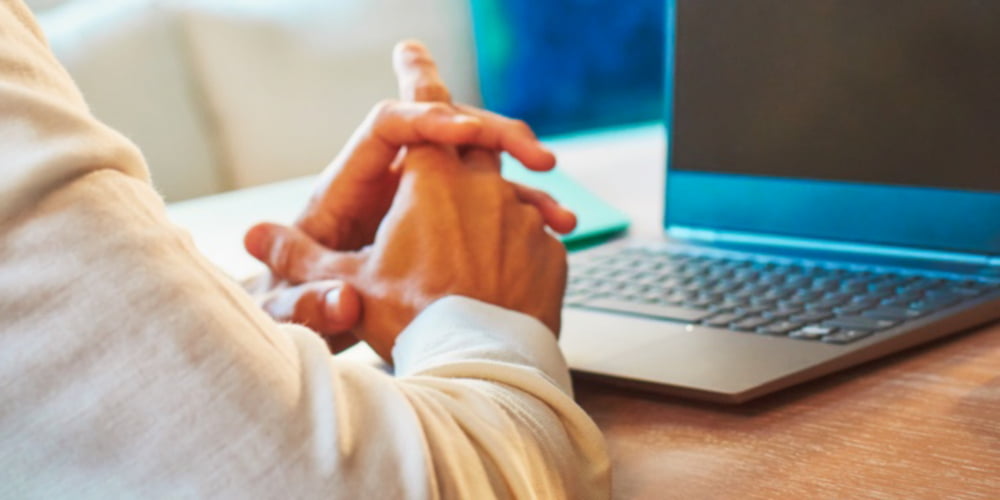 Folded hands in front a laptop.