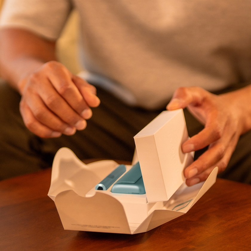 A woman looking at the back of an IQOS box. 