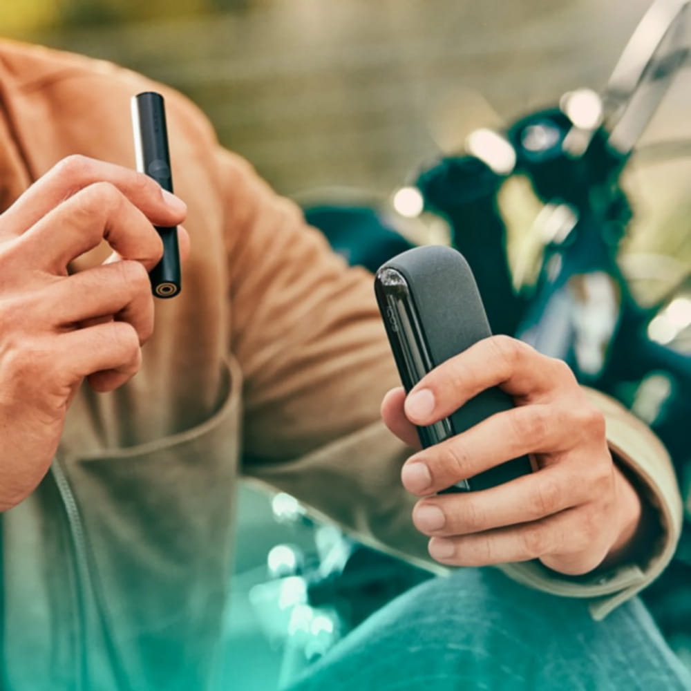 شخص يحمل شاحن جيب وجهاز IQOS ILUMA.