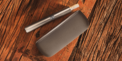 A passport, plane ticket, and IQOS device on a desk.