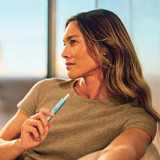 A woman holding an IQOS device while looking at her mobile phone.